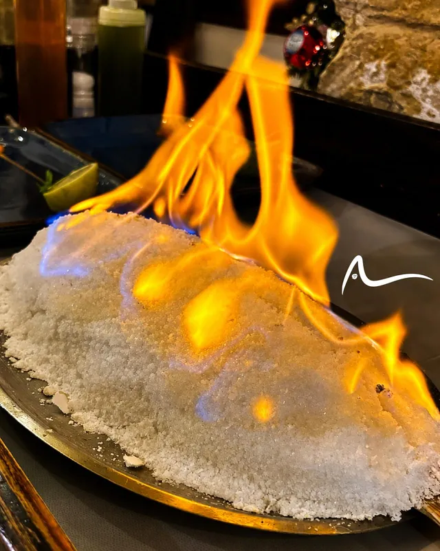 A fish baked in a salt crust, alight on a brass tray at the table