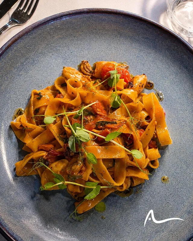 Tagliatelle with seafood in a tomato sauce, finished with pea shoots, in a blue speckled bowl