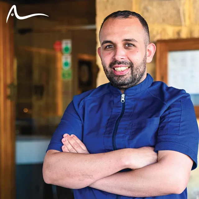 A chef in a blue Acqua Blu jacket, arms folded, photographed in the restaurant doorway