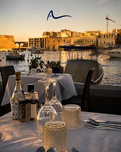 A terrace table dressed in white linen at sunset, the harbour behind